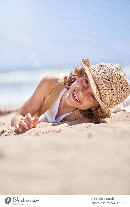 Lächelnder Junge auf sandigem Mantel in den Sommerferien niedlich Lügen ruhen Meeresufer Strand Barfuß Resort sorgenfrei Seeküste Urlaub wenig Küste Kind Glück