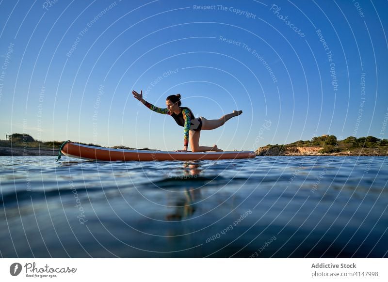 Ruhige Frau, die Yoga in der Balancing Table Pose macht Gleichgewicht Balanciertisch-Pose MEER Paddelbrett Surfer Konzentration Windstille Sonnenuntergang