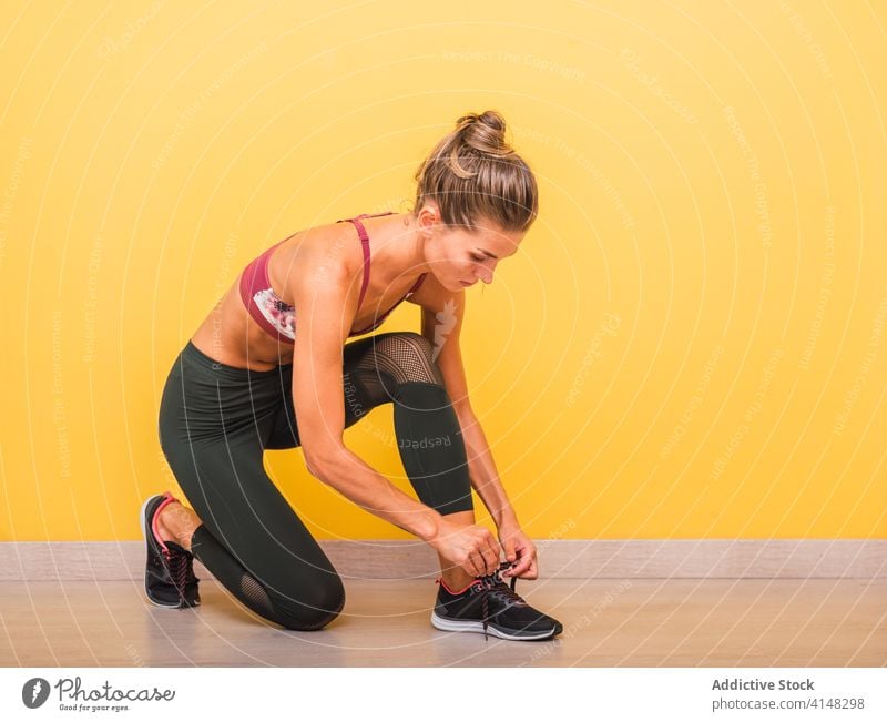 Fitte Frau beim Schnürsenkelbinden im Fitnessstudio Krawatte Schuhbänder Sportlerin Training Turnschuh Leggings selbstbewusst modern passen schlank BH