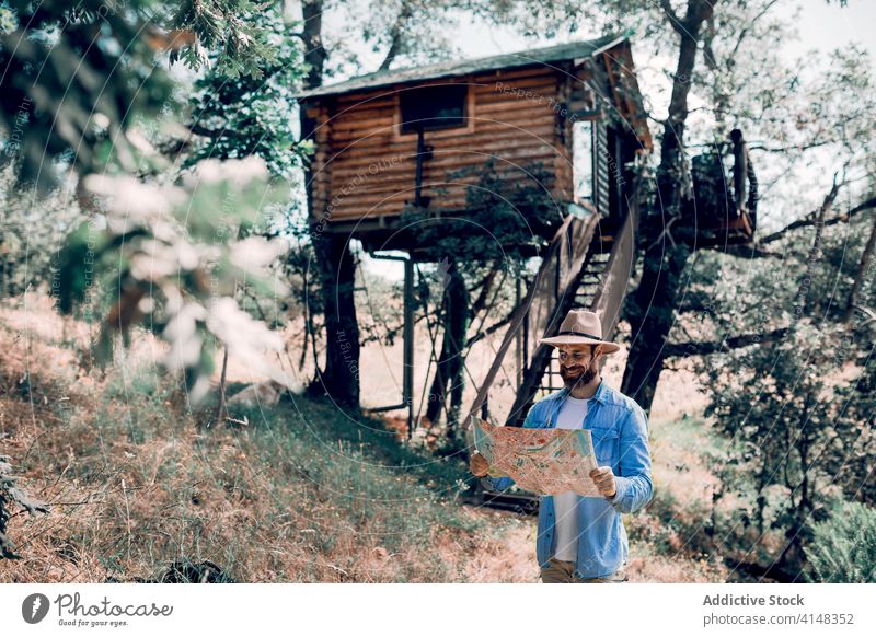 Fröhlicher Reisender, der sich auf einer Karte im Wald orientiert finden Örtlichkeit Landkarte sich orientieren Mann Papier navigieren Tourist Hütte männlich