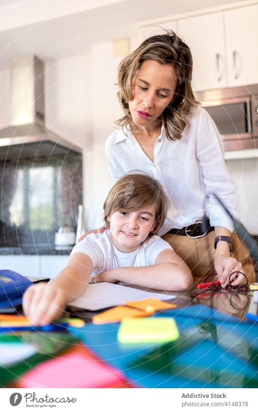 Geschäftsfrau überprüft Hausaufgaben, während sie in der Nähe des positiven Sohnes zu Hause steht Mutter prüfen Junge lernen Bildung Aufgabe heimisch Kindheit