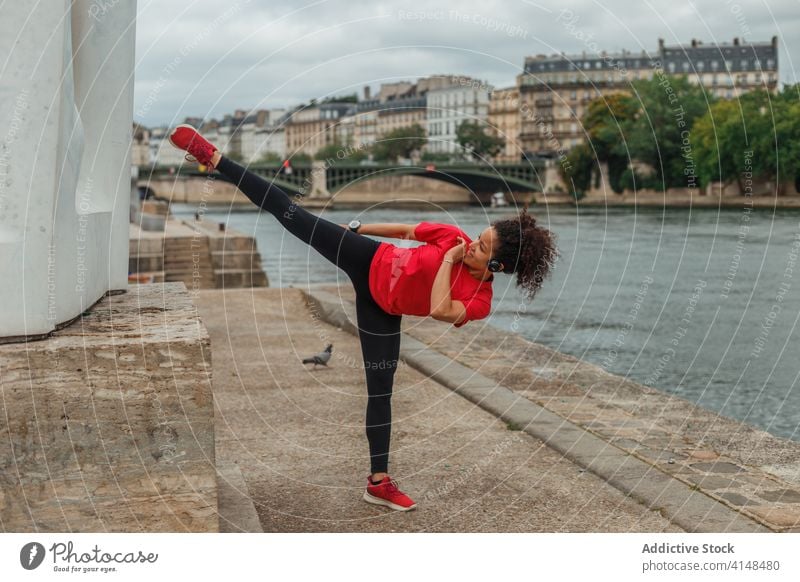 Ethnischer Athlet macht Karatekick auf dem Bürgersteig in der Nähe des Stadtflusses Sportlerin Kick Training passen beweglich Gleichgewicht intelligente Uhr