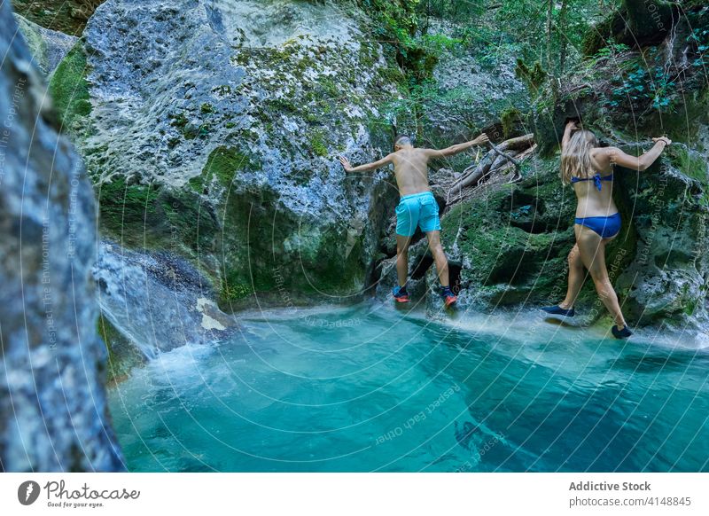 Reisendes Paar beim Überqueren eines Flusses im Sommer Aufstieg Klippe Felsen reisen Abenteuer felsig Wald Berghang Badebekleidung Feiertag Aktivität Freiheit