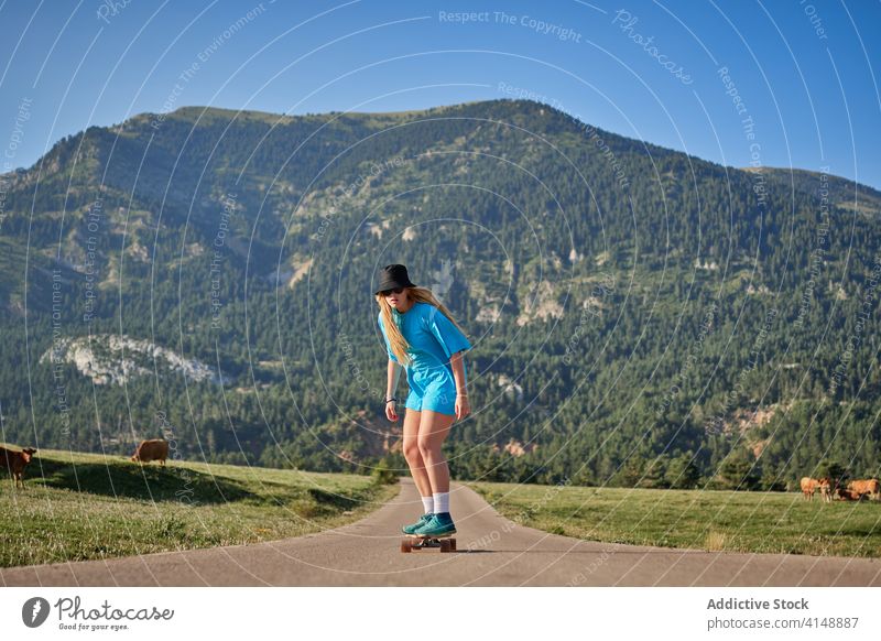 Frau fährt Skateboard entlang der Straße in den Bergen Skater Mitfahrgelegenheit Hipster Berge u. Gebirge Sommer jung Schlittschuh Wochenende ländlich Sport