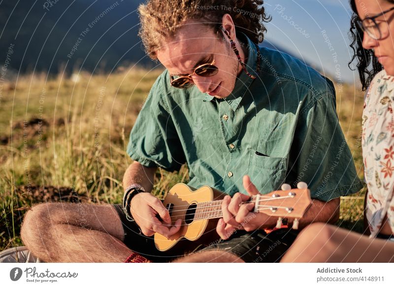 Zufriedene Freunde, die gemeinsam in den Bergen entspannen spielen Ukulele sich[Akk] entspannen Zusammensein Berge u. Gebirge Hipster unterhalten Browsen