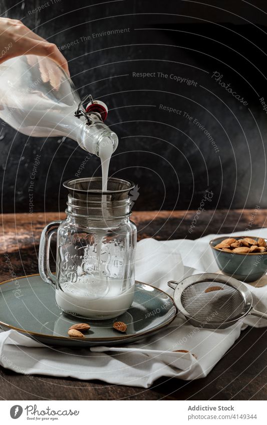 Person, die Mandelmilch in ein Glas gießt eingießen melken Veganer rustikal Sieb Teller Stoff Tisch trinken Getränk Vegetarier Flasche natürlich Ernährung