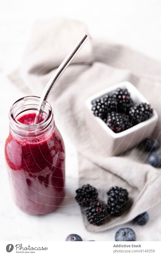 Vertikale Nahaufnahme einer Glasflasche mit Beeren-Smoothie und einem Metallstrohhalm darin. Flasche abschließen Farbe trinken Essen und Trinken Früchte