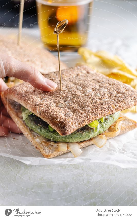 Crop Person mit leckerem Sandwich Vegetarier Belegtes Brot Café Zuprosten Bier Snack Gemüse schmackhaft Kotelett Tisch Glas Lebensmittel Getränk Mittagessen