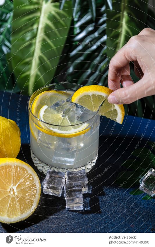 Crop Person mit Glas Zitronencocktail Cocktail Alkohol Erfrischung Garnierung Getränk Scheibe dienen kalt cool Eis Würfel Tisch Frucht Zitrusfrüchte liquide