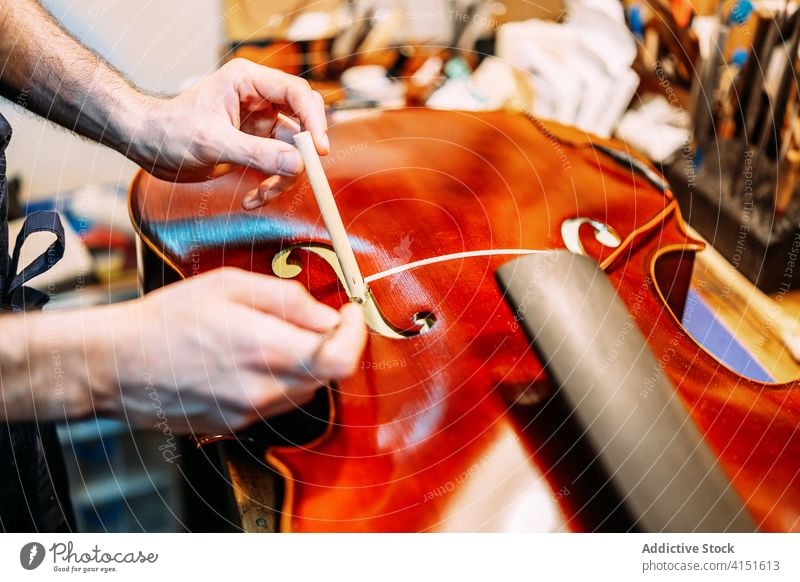 Anonymer Geigenbauer beim Einbau des Stimmstocks in die Geige Zupfinstrumentenmacher Klang einstecken installieren machen Instrument Kunstgewerbler Handwerk