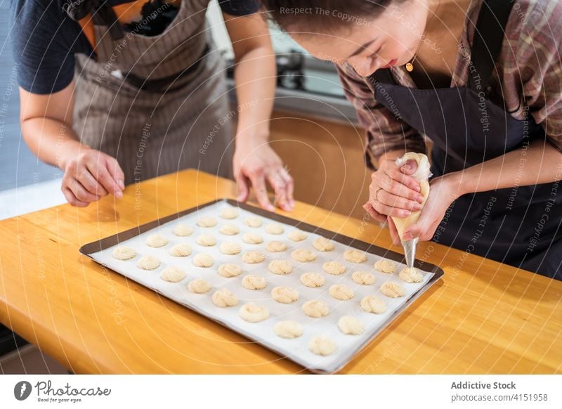 Junge Bäcker beim gemeinsamen Backen in der Küche Paar Bäckerei heimwärts Teamwork Gebäck Spritzbeutel Röhren Backwarenbeutel Teig Teigwaren Zusammensein Spaß