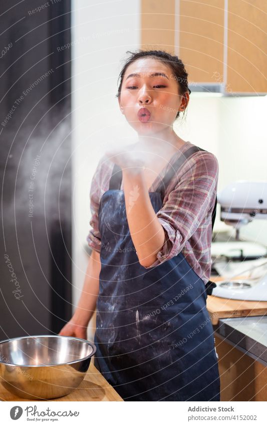 Verspielter Bäcker bläst Mehlstaub Frau spielerisch Staubwischen Schlag Air Spaß Glück heimwärts Küche Schürze Pulver heiter Tisch Freude Gebäck Bestandteil