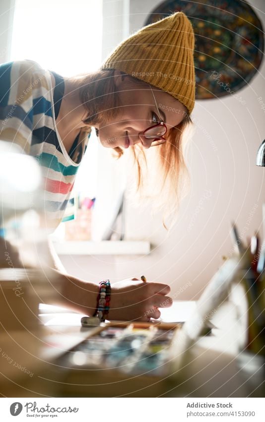 Fröhliche Frau malt in der Werkstatt Künstler Farbe Wasserfarbe kreieren Handwerkerin heiter Fähigkeit Anstreicher Kunstwerk Hobby Inspiration trendy Atelier