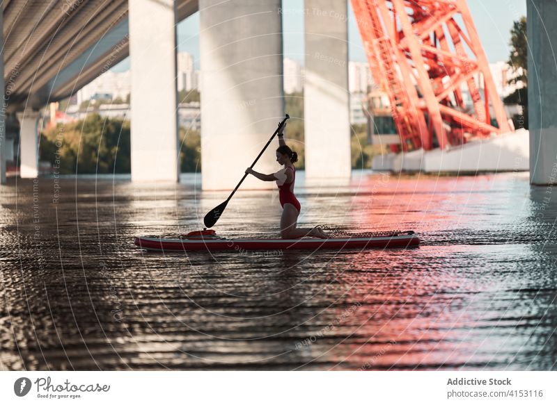 Weibliche Surferin schwimmt auf einem Paddelbrett Frau Reihe Brandung Surfbrett Fluss Brücke Großstadt Wasser Sommer Aktivität Sport Stadtbild Hobby Gerät