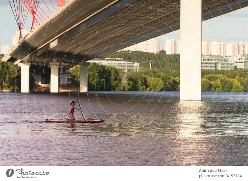 Weibliche Surferin schwimmt auf einem Paddelbrett Frau Reihe Brandung Surfbrett Fluss Brücke Großstadt Wasser Sommer Aktivität Sport Stadtbild Hobby Gerät