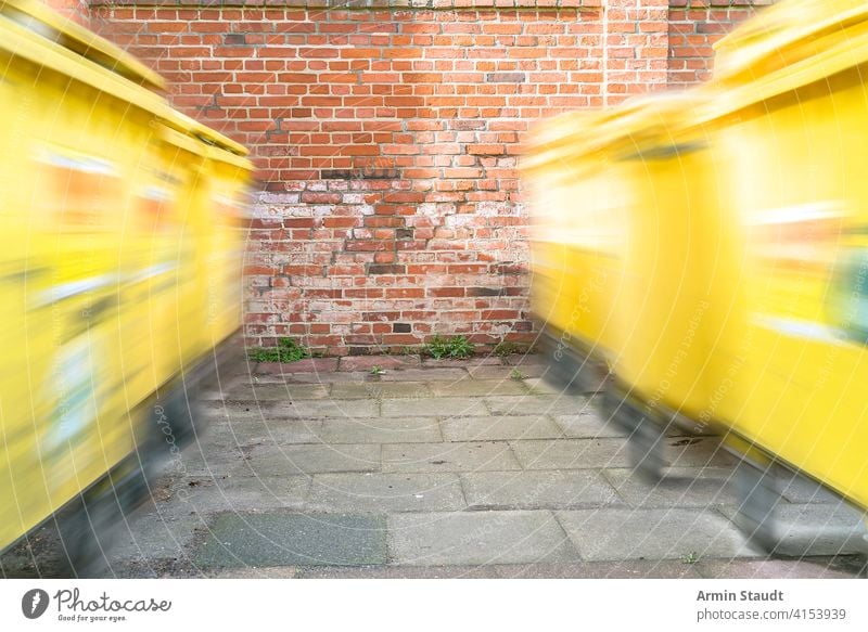 Bewegender gelber Müllcontainer vor einer roten Ziegelwand Behälter Unschärfe Erhaltung Container Müllhalde Mülltonne Umwelt umgebungsbedingt Zaun Garten Gate