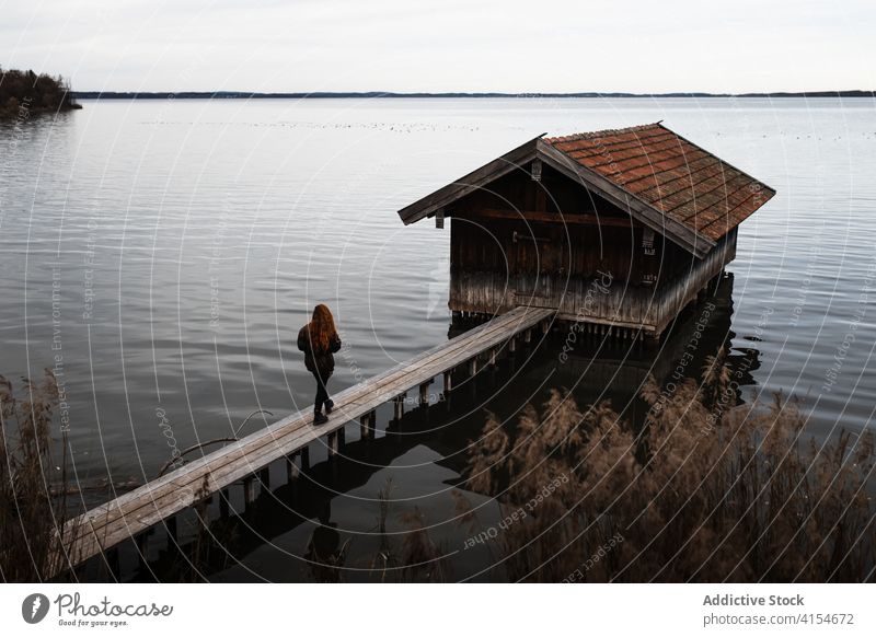 Einsame Frau steht auf Holzsteg am See Pier Baracke Herbst trist einsam Reisender schäbig Windstille ruhig Natur reisen Tourismus Deutschland Österreich hölzern