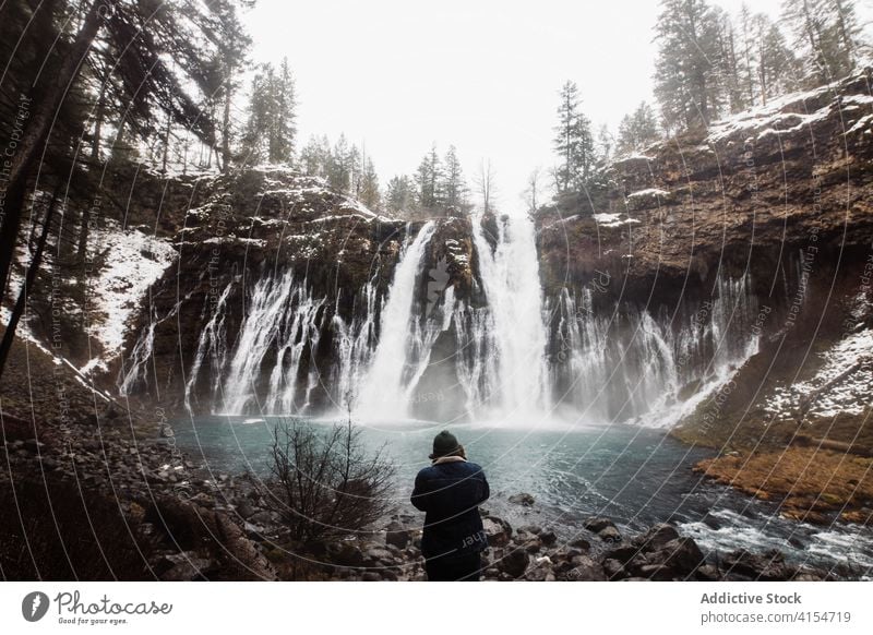 Anonyme Person an einem Wasserfall in einem verschneiten Bergwald an einem Wintertag Wald Schnee fließen Natur Landschaft Pool kalt strömen malerisch reisen