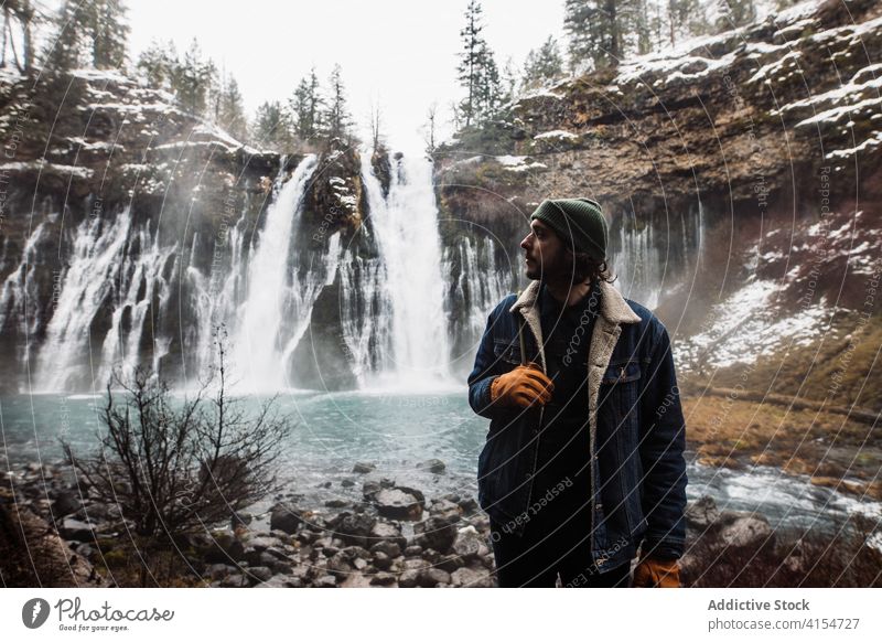 Männlicher Reisender auf Wasserfall in verschneiten bergigen Wald im Winter Tag Mann Schnee fließen Natur Person Landschaft Pool männlich kalt strömen malerisch