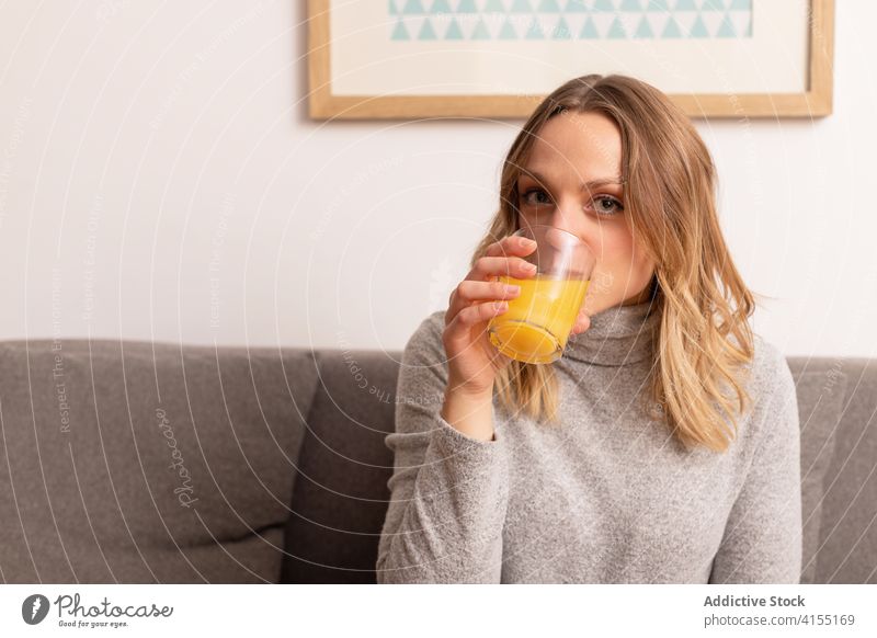 Fröhliche Frau trinkt frischen Orangensaft zu Hause Lächeln heimwärts Liege online Job Komfort Glück Sofa sitzen Glas orange Saft Wohnzimmer Appartement froh