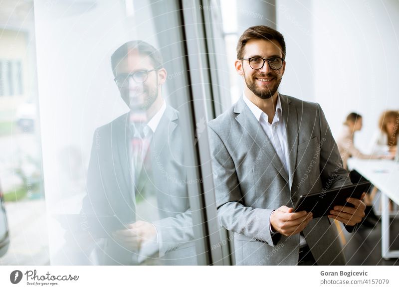 Junger moderner Geschäftsmann mit digitalem Tablet im Büro Vollbart Business Unternehmen korporativ Mitarbeiter Brille finanziell gutaussehend im Innenbereich