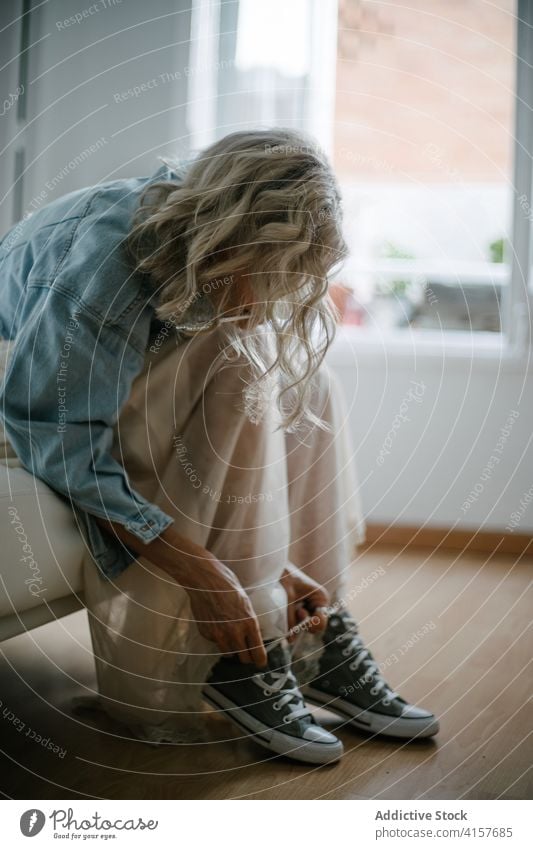 Frau bindet zu Hause die Schnürsenkel ihrer Turnschuhe Schnüffler Krawatte Schuhbänder Stil trendy heimwärts Appartement Schuhe Rock Jeansstoff Jacke Sofa