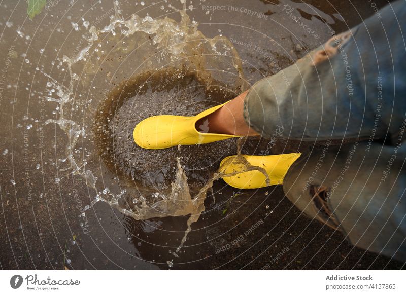 Luftaufnahme der gelben Regenstiefel, die auf eine Pfütze treffen und Wasser verspritzen Schritt Witz Unschuld Lebensstile unordentlich Antenne spielerisch