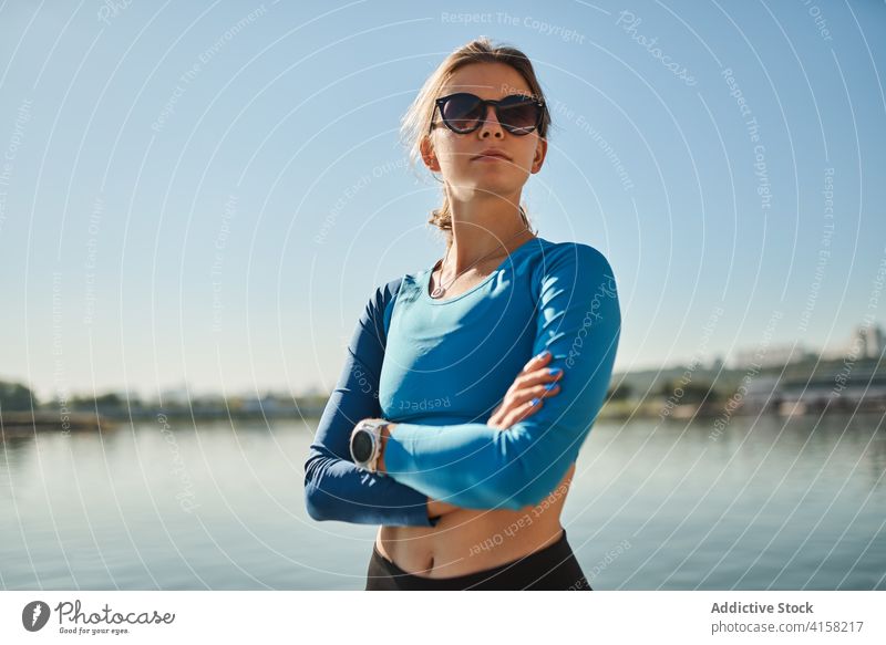 Schlanke aktive Frau in Sportkleidung und Sonnenbrille steht in der Nähe von Fluss sportlich selbstbewusst passen schlank Training Fitness Tracker