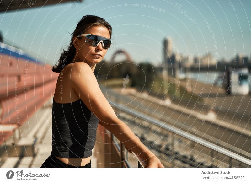 Junge Frau in Sportkleidung und mit Sonnenbrille steht im Stadion sportlich Brille passen aktiv selbstbewusst trendy Stil Mode jung modern schlank