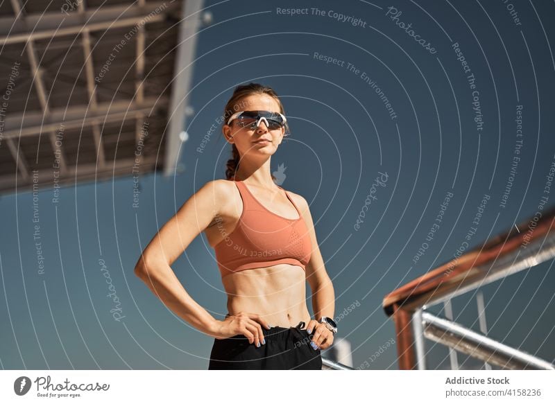 Junge Frau in Sportkleidung und mit Sonnenbrille steht im Stadion sportlich Brille passen aktiv selbstbewusst trendy Stil Mode jung modern schlank