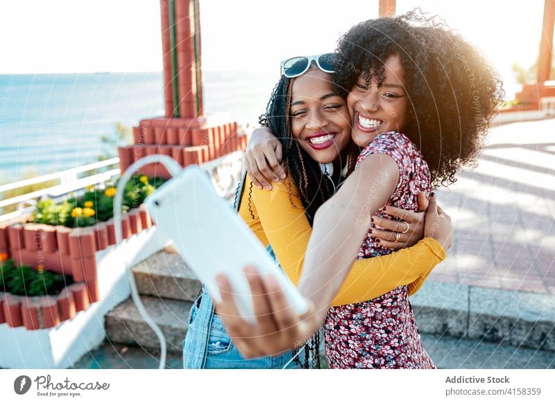 Fröhliche schwarze Freunde nehmen Selfie in der Stadt Umarmung Smartphone Frauen Freundschaft heiter Bonden benutzend Sommer Spazierweg ethnisch Afroamerikaner