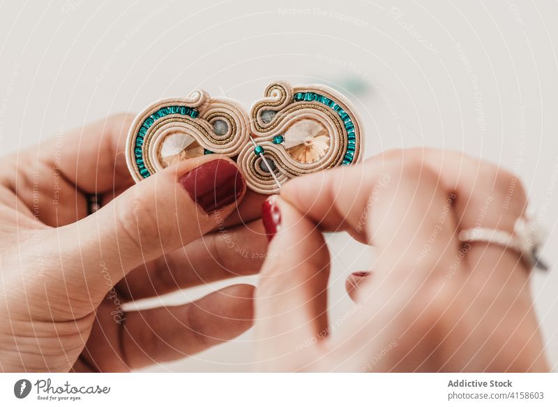 Unerkennbarer Kunsthandwerker bei der Herstellung von Soutache-Ohrringen im Atelier Bijouterie Frau kreieren handgefertigt Werkstatt Prozess Handwerk kreativ