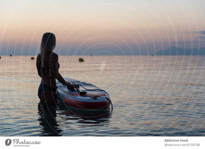 Anonyme Frau übt in der Nähe von Paddleboard bei Sonnenuntergang Paddelbrett Surfer Zusatzplatine Reihe MEER Training Surfbrett Sommer Holzplatte sportlich