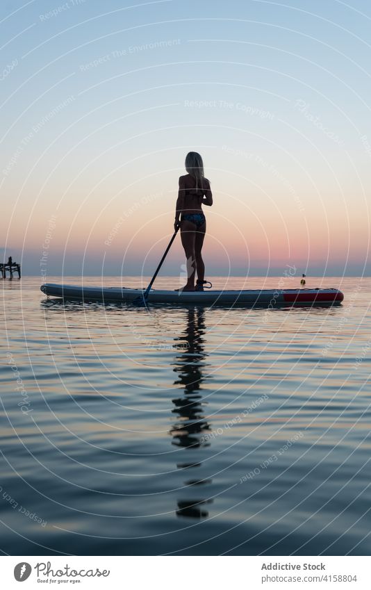 Anonyme Frau übt auf Paddleboard bei Sonnenuntergang Paddelbrett Surfer Zusatzplatine Silhouette Reihe MEER Training Surfbrett Sommer Holzplatte sportlich