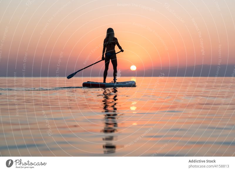 Anonyme Frau übt auf Paddleboard bei Sonnenuntergang Paddelbrett Surfer Zusatzplatine Silhouette Reihe MEER Training Surfbrett Sommer Holzplatte sportlich