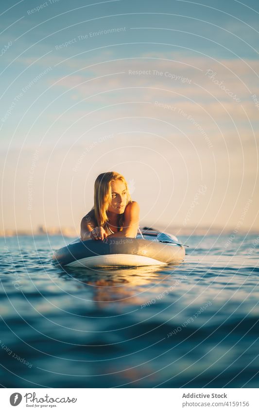 Gelassene Frau auf Surfbrett im Meer Lügen MEER sich[Akk] entspannen Sonnenuntergang schlank Badeanzug Wasser winken Himmel Erholung Sommer Badebekleidung ruhen