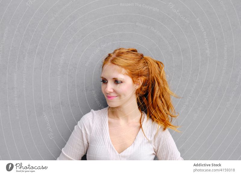 Junge rothaarige Frau steht in der Nähe von grauen Wand rote Haare urban Kleid Stil positiv trendy jung Rotschopf Lächeln selbstbewusst Zeitgenosse Mode Inhalt