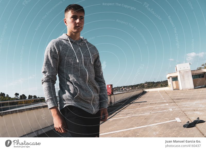 Ein Teenager mit kurzen Haaren macht eine Pause vom Skateboardfahren auf einem verlassenen Parkplatz Verlassen Sweatshirt abgestufter Haarschnitt allein