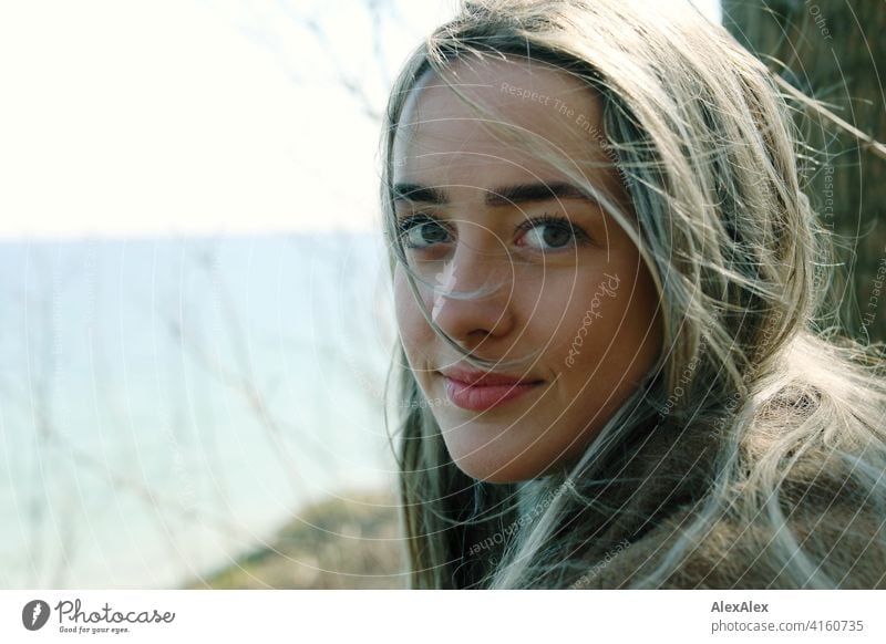 Ein schönes blondes Mädchen steht am Ostseestrand an der Steilküste und schaut zurück in die Kamera Lächeln freudig Landschaft von Freude Außenaufnahme Gesicht