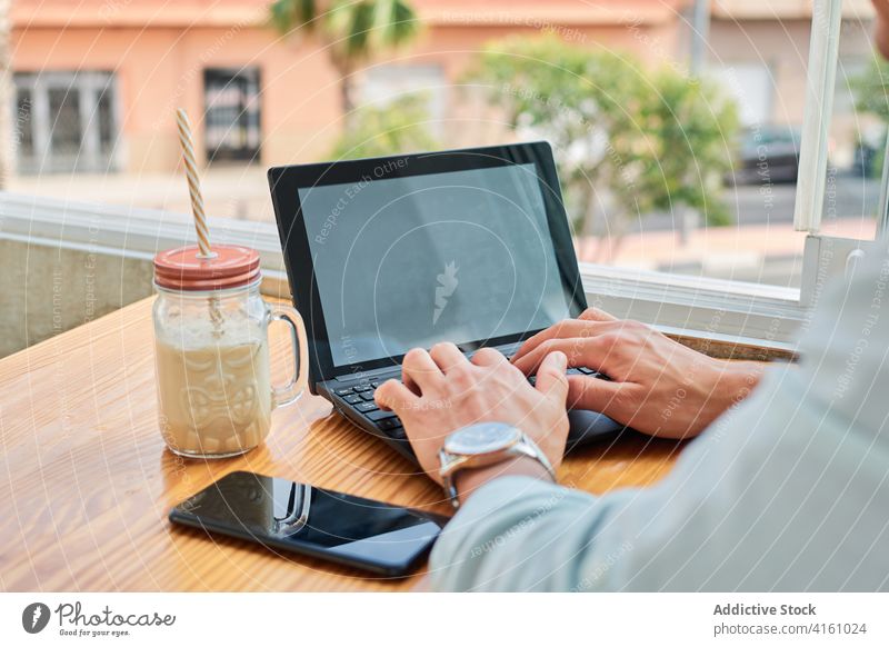 Crop-Mann arbeitet ferngesteuert am Netbook im Café Arbeit Laptop freiberuflich Tippen Getränk Smartphone Anschluss Job Internet online männlich jung Browsen