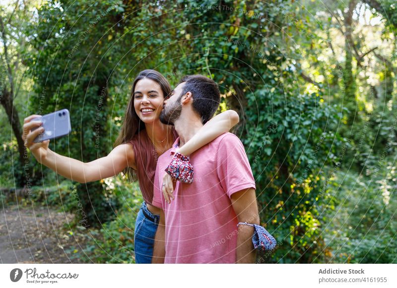 Fröhliches ethnisches Paar nimmt Selfie im Park Kuss Glück Smartphone kuscheln Termin & Datum romantisch Liebe Zusammensein Partnerschaft Apparatur Mobile