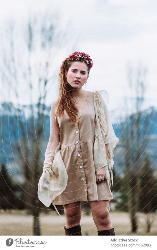 Modische Frau in trendigem Outfit und Kranz im Bergwald stehend Mode Stil Boho nordisch Totenkranz Berge u. Gebirge Schnee Wald Natur selbstbewusst jung Kleid