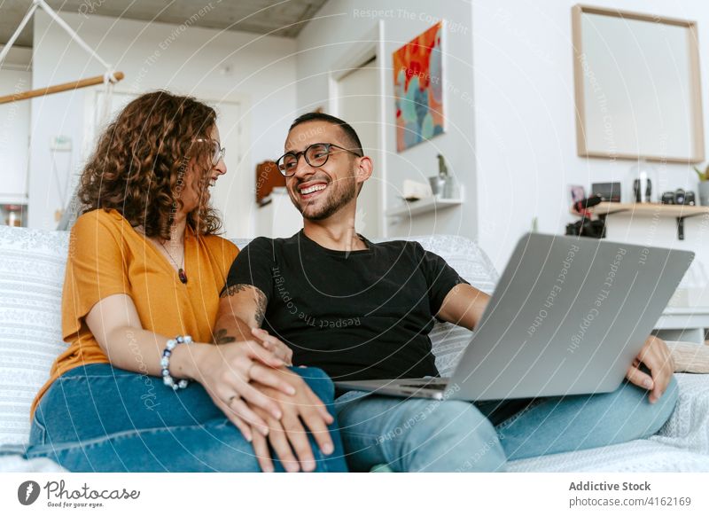 Glückliches Paar mit Video-Gespräch auf Laptop zu Hause Videoanruf Zusammensein Händchenhalten Sofa heimwärts Wellenhand heiter Anschluss Partnerschaft Freund