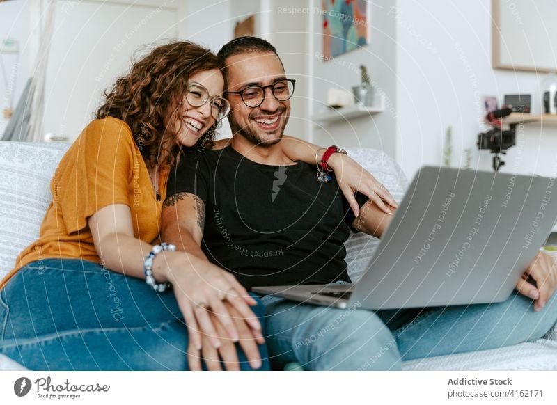 Glückliches Paar mit Video-Gespräch auf Laptop zu Hause Videoanruf Zusammensein Händchenhalten Sofa heimwärts Wellenhand heiter Anschluss Partnerschaft Freund