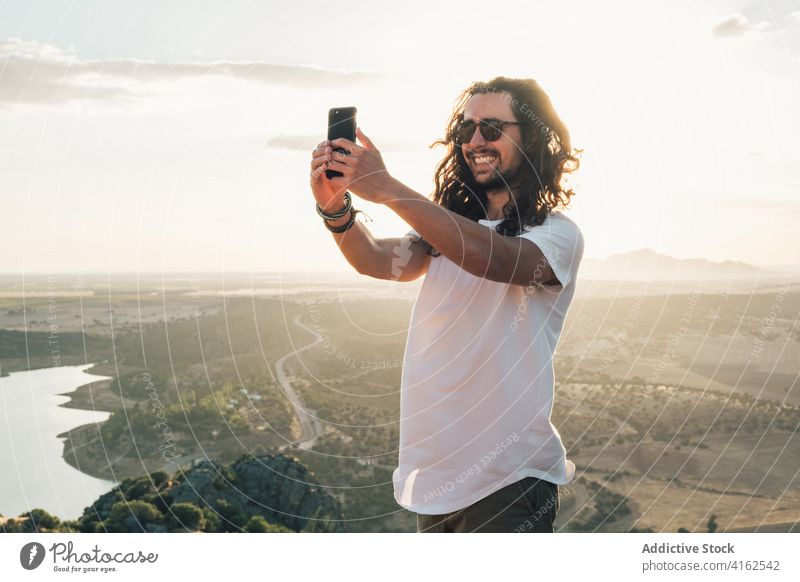 Fröhlich Mann unter Selfie gegen sonnigen üppigen Tal Reisender heiter Zahnfarbenes Lächeln Smartphone Natur aufgeregt Moment Apparatur Bergkuppe Fernweh reisen