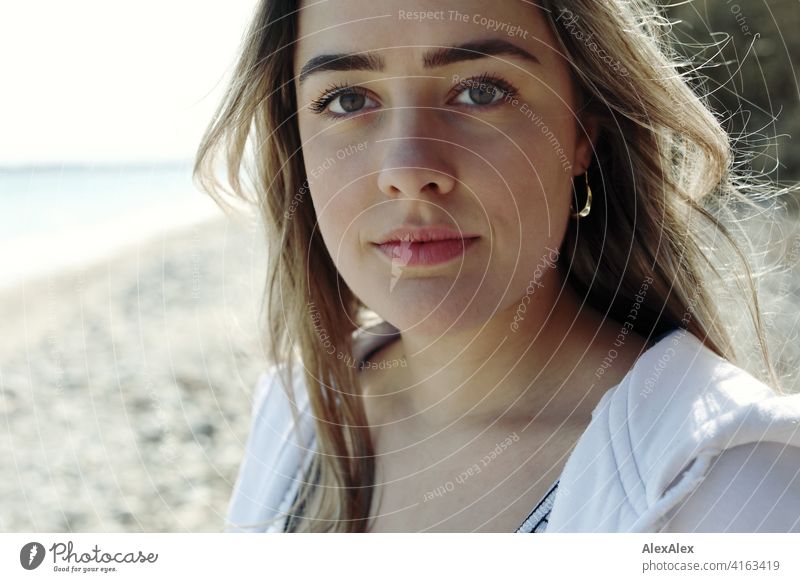 Ein schönes blondes Mädchen steht am Ostsee- Strand und schaut in die Kamera Lächeln freudig Landschaft Aus Freude Außenaufnahme Gesicht Junge Frau hübsch