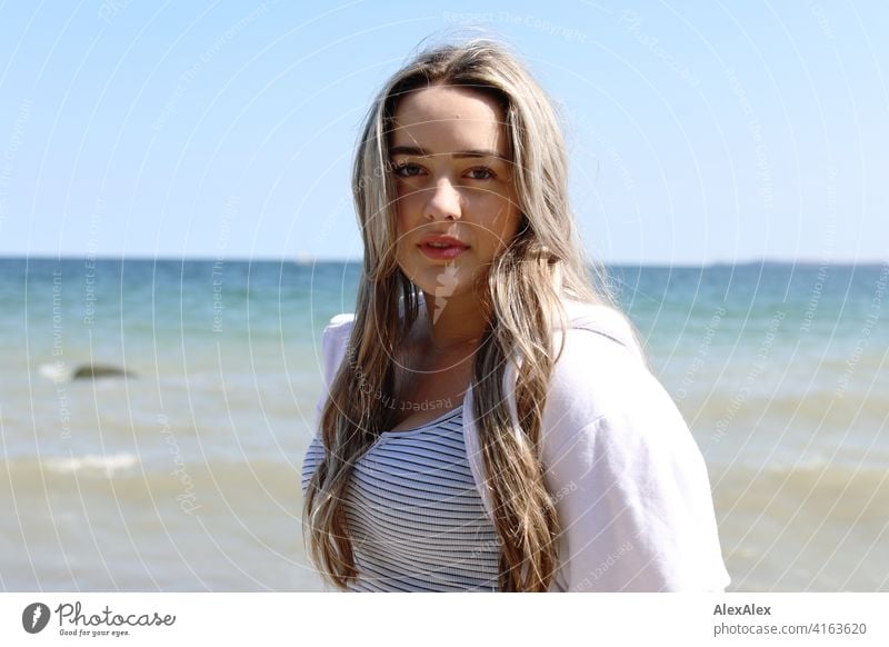 Ein schönes blondes Mädchen steht am Ostseestrand und schaut in die Kamera Lächeln freudig Landschaft von Freude Außenaufnahme Gesicht Junge Frau hübsch