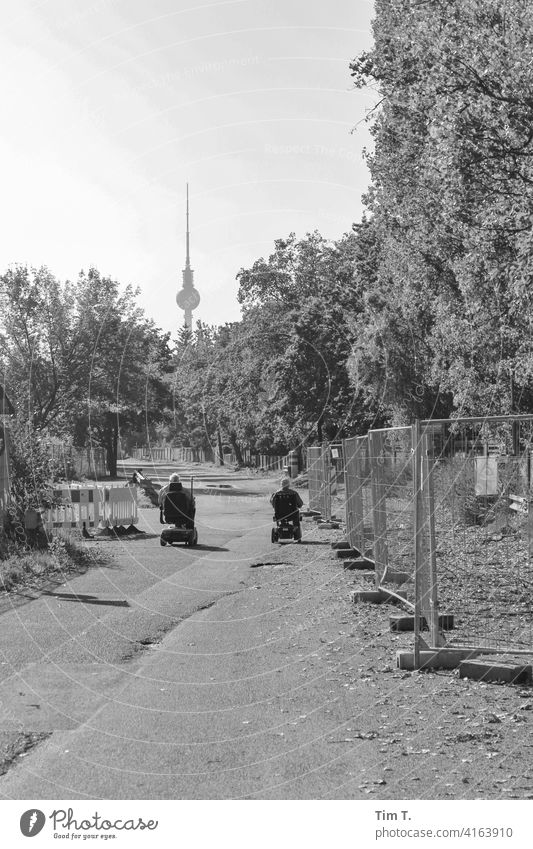 zwei Männer fahren im E-Rollstuhl durch den Mauerpark dem Fernsehturm entgegen mauerpark Prenzlauer Berg bnw s/w Berlin Hauptstadt Stadtzentrum Außenaufnahme