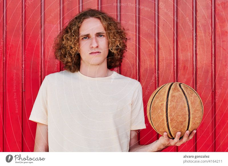 ein junger Mann mit lockigem Haar und grünen Augen, der mit einem Basketball in der Hand in die Kamera schaut che Ball Person Korb Sport sportlich männlich