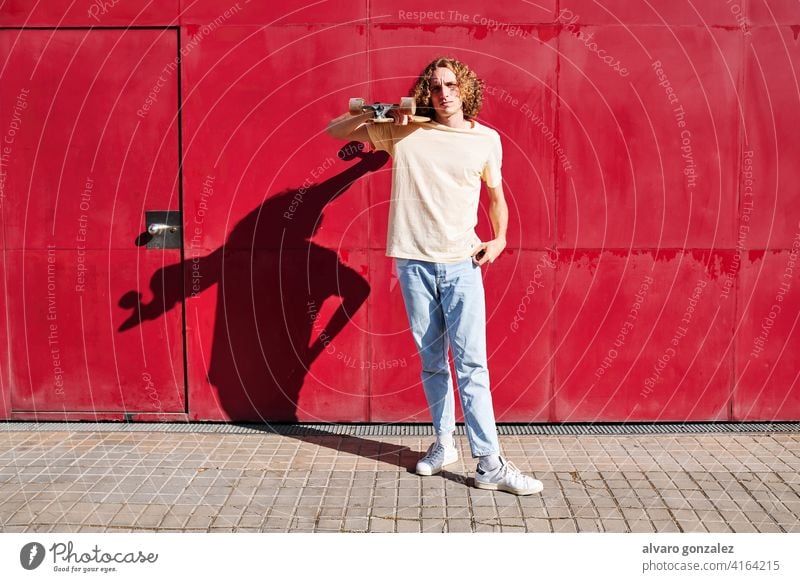 ein junger Mann mit lockigem Haar und seinem Skateboard mit rotem Hintergrund an einem sonnigen Sommertag Basketball Ball Person Korb Sport sportlich männlich